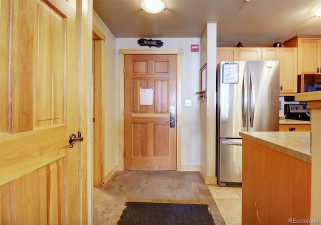 kitchen with light carpet, stainless steel appliances, light countertops, light brown cabinetry, and light tile patterned flooring