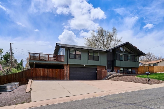 split foyer home featuring fence, an attached garage, central AC, brick siding, and concrete driveway