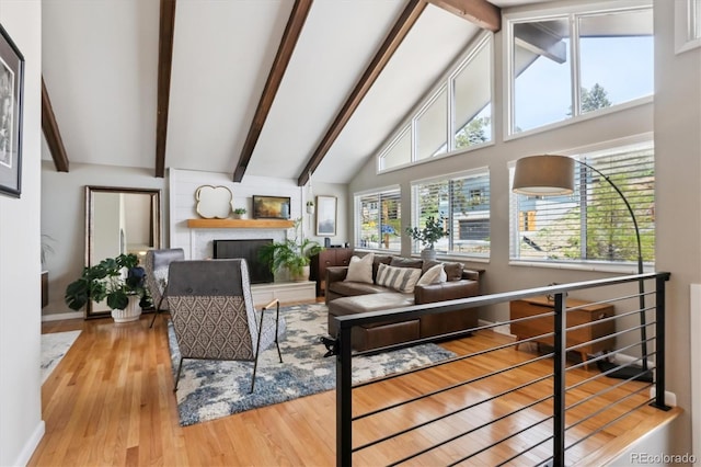 living room with a fireplace with raised hearth, high vaulted ceiling, wood finished floors, and beam ceiling