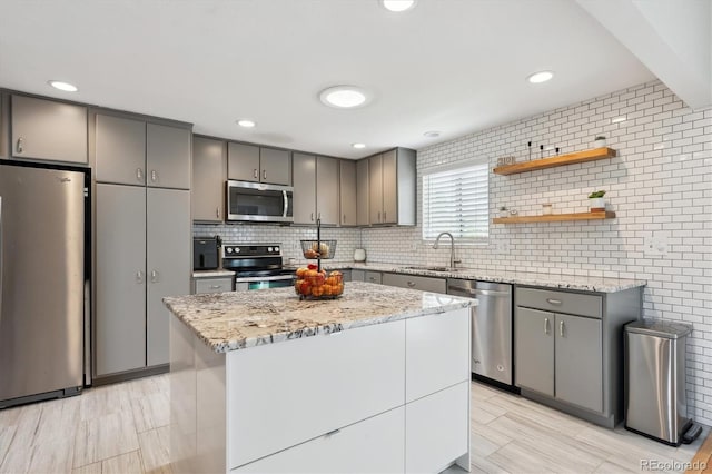 kitchen featuring decorative backsplash, light stone countertops, a sink, appliances with stainless steel finishes, and gray cabinetry