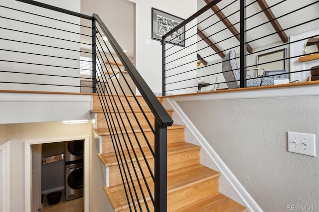 stairway featuring stacked washer and dryer, a textured wall, a towering ceiling, and wood finished floors