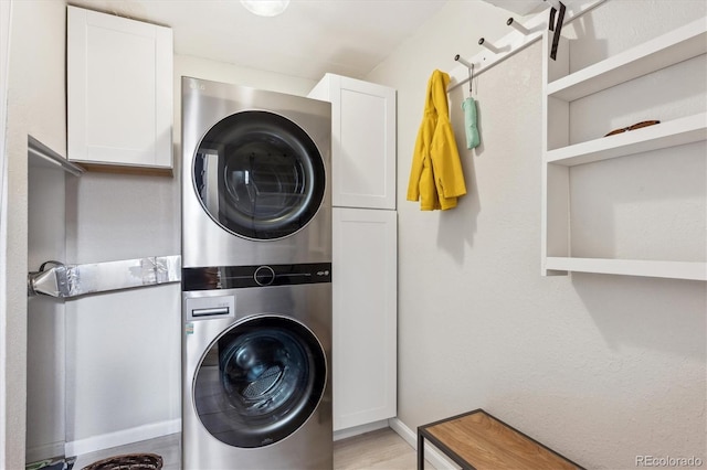 laundry area featuring stacked washer / drying machine, light wood finished floors, and cabinet space