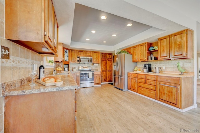 18045 Sunburst Dr, Monument, CO 80132 - kitchen featuring stainless steel appliances, a raised ceiling, a sink, light wood-style floors, and decorative backsplash