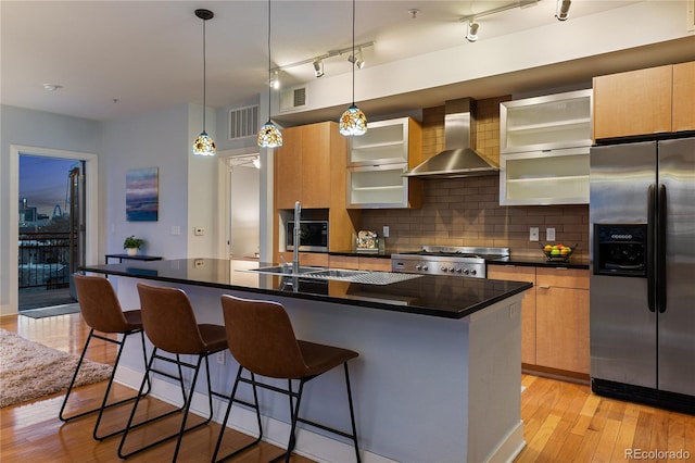 kitchen featuring dark countertops, stainless steel fridge with ice dispenser, light wood-style flooring, wall chimney exhaust hood, and range