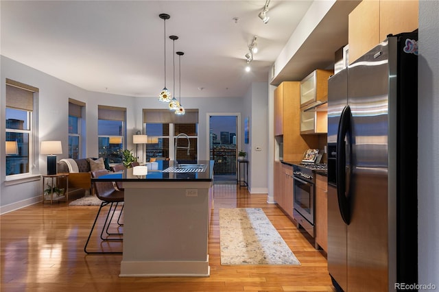 kitchen with light wood-style floors, dark countertops, appliances with stainless steel finishes, and an island with sink