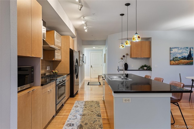 kitchen featuring fridge with ice dispenser, an island with sink, a sink, dark countertops, and stainless steel range with gas stovetop