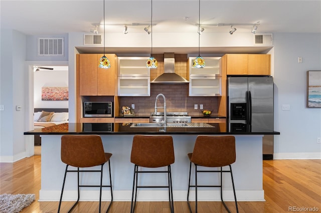 kitchen with visible vents, stainless steel appliances, a breakfast bar area, wall chimney exhaust hood, and decorative backsplash