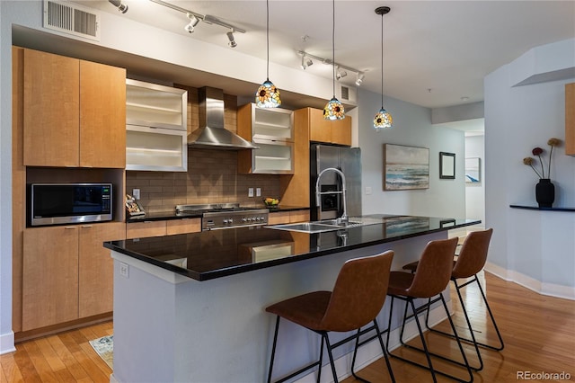 kitchen with light wood finished floors, visible vents, wall chimney range hood, appliances with stainless steel finishes, and a kitchen breakfast bar