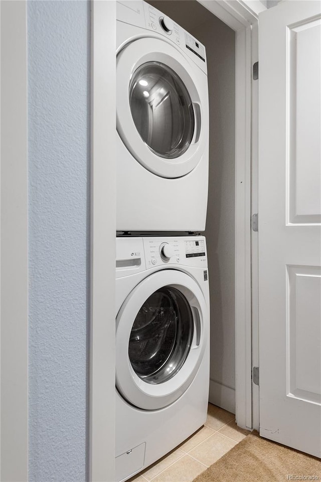 washroom with laundry area, stacked washer and dryer, light tile patterned flooring, and a textured wall