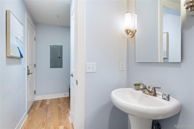 bathroom featuring electric panel, baseboards, wood finished floors, and a sink