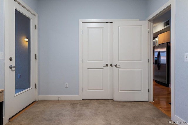 unfurnished bedroom featuring a closet, carpet floors, visible vents, and stainless steel fridge with ice dispenser