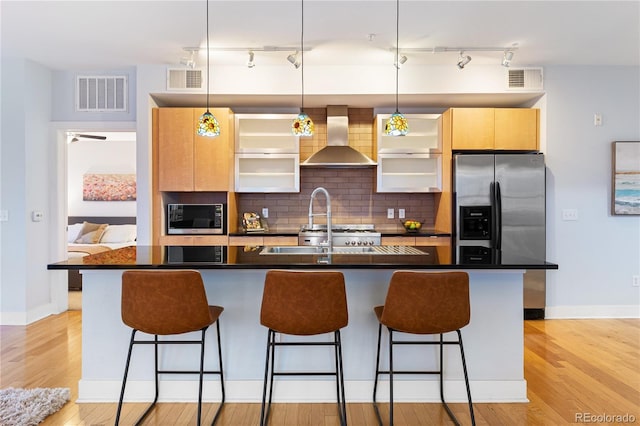 kitchen with wall chimney exhaust hood, visible vents, a breakfast bar, dark countertops, and stainless steel appliances