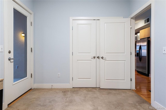 unfurnished bedroom featuring a closet, stainless steel refrigerator with ice dispenser, light colored carpet, and visible vents