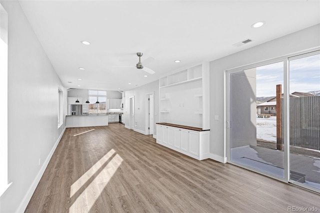 unfurnished living room featuring light hardwood / wood-style floors, built in shelves, and ceiling fan