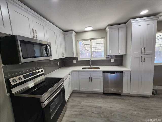 kitchen with light wood-type flooring, appliances with stainless steel finishes, white cabinets, and sink