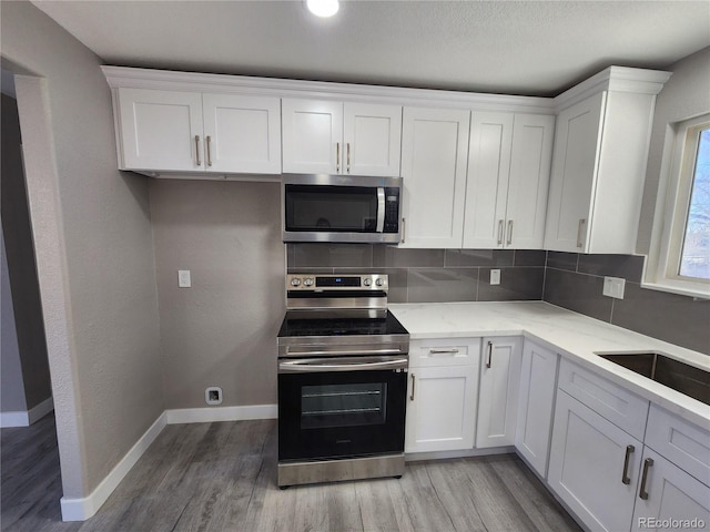 kitchen featuring decorative backsplash, white cabinetry, light wood-type flooring, appliances with stainless steel finishes, and light stone counters