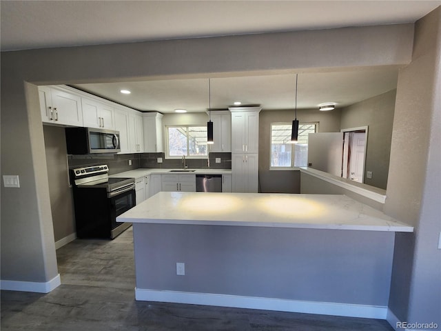 kitchen with white cabinetry, appliances with stainless steel finishes, kitchen peninsula, and hanging light fixtures