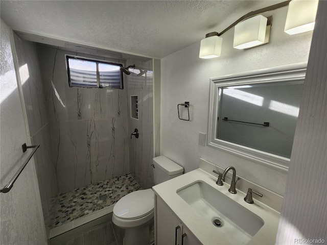 bathroom with toilet, a tile shower, tile patterned flooring, a textured ceiling, and vanity