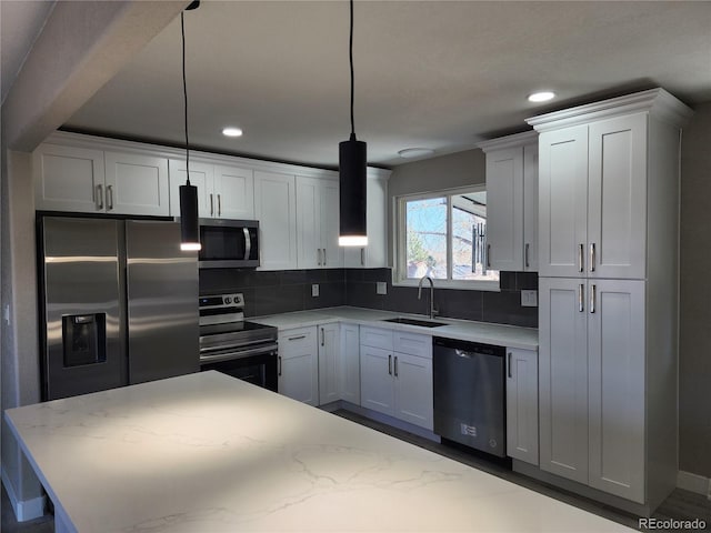 kitchen with pendant lighting, white cabinetry, sink, light stone counters, and stainless steel appliances