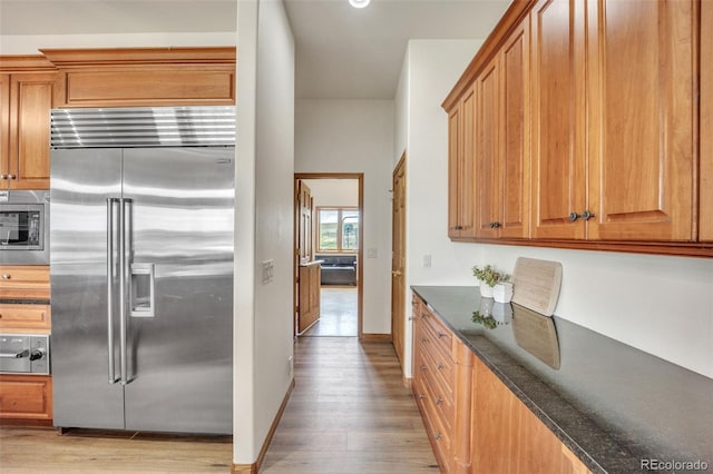 15125 Spring Valley Rd, Larkspur, CO 80118 - kitchen featuring built in appliances, light wood finished floors, dark stone counters, and brown cabinetry