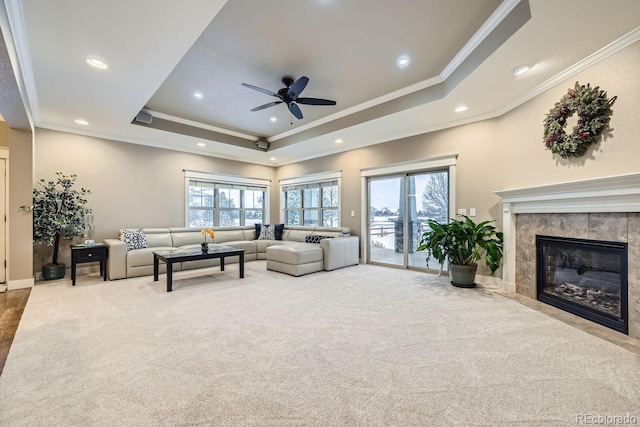 carpeted living room with a tiled fireplace, crown molding, a wealth of natural light, and a tray ceiling