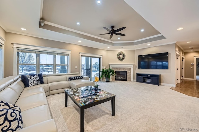 carpeted living room featuring crown molding, a fireplace, a raised ceiling, and ceiling fan