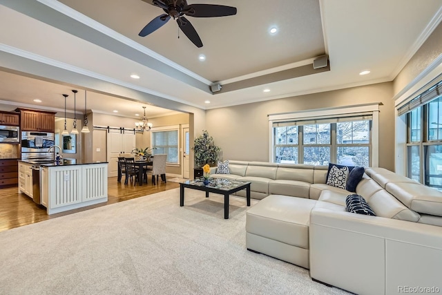 living room featuring sink, crown molding, a tray ceiling, light hardwood / wood-style floors, and ceiling fan with notable chandelier