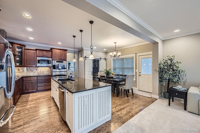 kitchen featuring sink, decorative light fixtures, appliances with stainless steel finishes, an island with sink, and a barn door