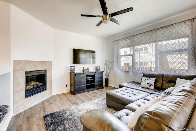 living room featuring a tiled fireplace, ceiling fan, and light wood-type flooring