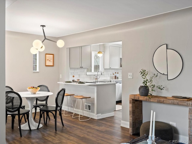 kitchen featuring dark wood-type flooring, a breakfast bar area, decorative light fixtures, kitchen peninsula, and decorative backsplash