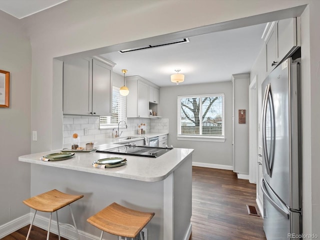 kitchen featuring a peninsula, a sink, stainless steel appliances, light countertops, and backsplash