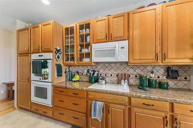 5289 Fairfield Cir, Castle Rock, CO 80104 - kitchen featuring white appliances, decorative backsplash, light stone countertops, glass insert cabinets, and a textured ceiling
