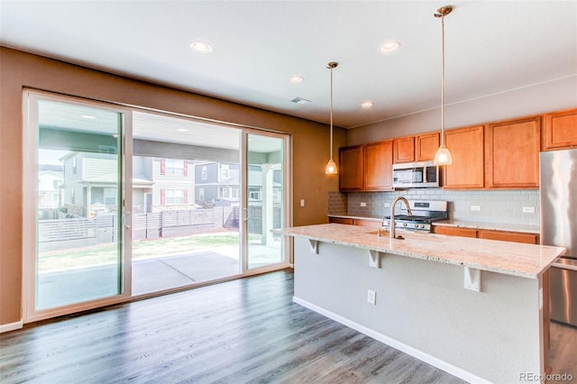 kitchen with backsplash, appliances with stainless steel finishes, light stone counters, and light wood finished floors