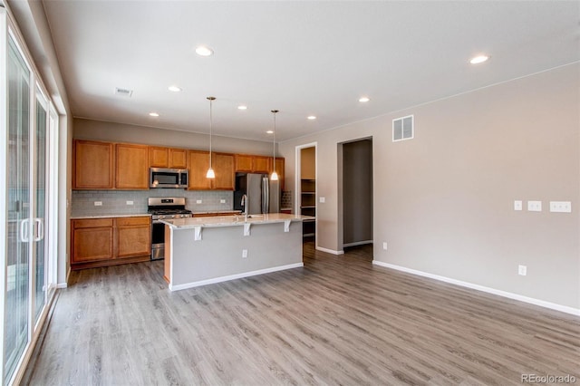 kitchen with tasteful backsplash, light wood-type flooring, a kitchen island with sink, visible vents, and appliances with stainless steel finishes