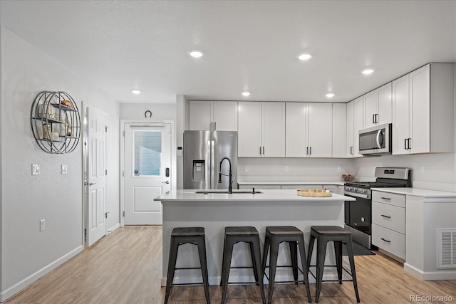 kitchen with light wood finished floors, a breakfast bar area, stainless steel appliances, light countertops, and a sink