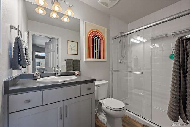 bathroom featuring visible vents, a textured wall, toilet, wood finished floors, and a shower stall