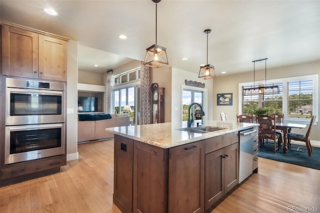17275 Gwilym Ct, Monument, CO 80132 - kitchen featuring appliances with stainless steel finishes, a sink, light wood finished floors, light stone counters, and hanging light fixtures