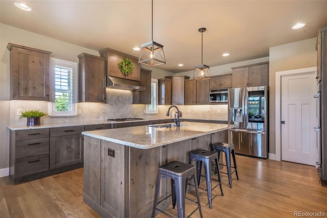 17275 Gwilym Ct, Monument, CO 80132 - kitchen with stainless steel appliances, a sink, under cabinet range hood, tasteful backsplash, and light wood finished floors
