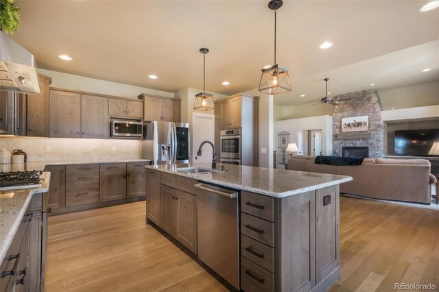 17275 Gwilym Ct, Monument, CO 80132 - kitchen featuring appliances with stainless steel finishes, a sink, ceiling fan, a stone fireplace, and light wood-style flooring