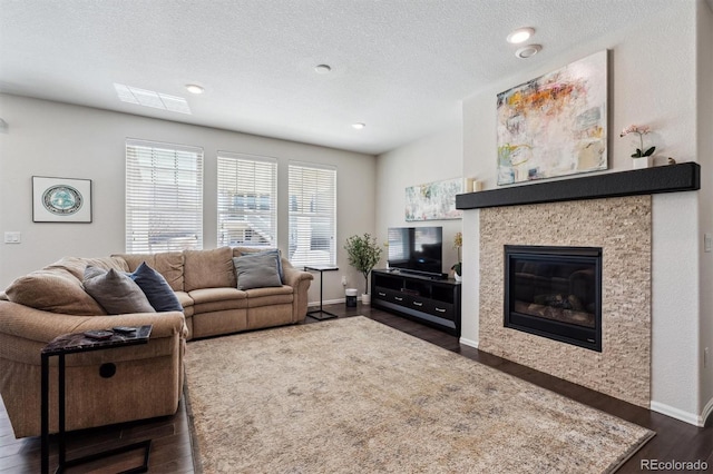 living area featuring a glass covered fireplace, dark wood-style flooring, a textured ceiling, and baseboards