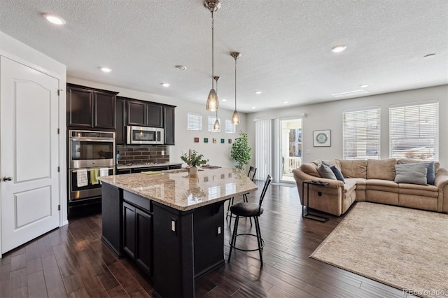 kitchen featuring stainless steel appliances, open floor plan, dark wood-type flooring, and a kitchen bar