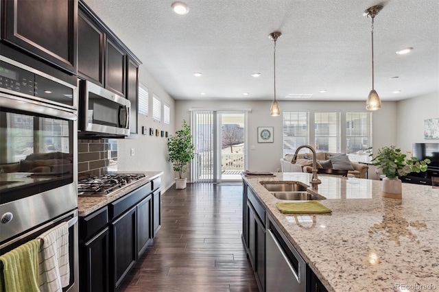 kitchen featuring light stone counters, appliances with stainless steel finishes, dark wood-type flooring, a sink, and backsplash