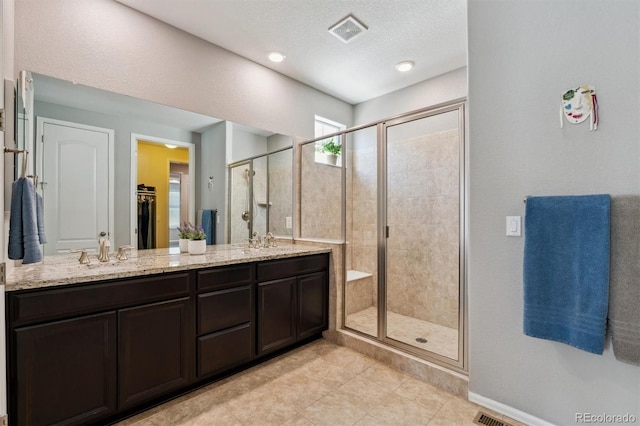 bathroom featuring double vanity, a stall shower, visible vents, a textured ceiling, and a sink