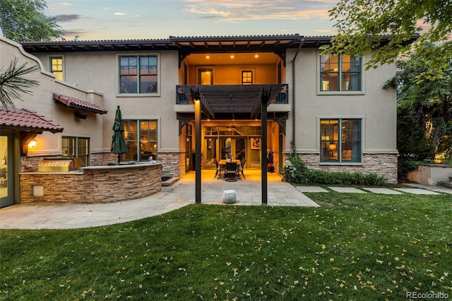 235 Eudora St, Denver, CO 80220 - back of house at dusk with stone siding, a balcony, stucco siding, and a yard