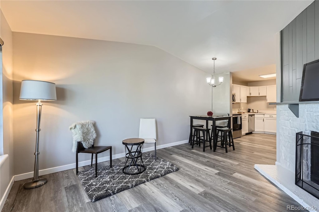 sitting room featuring an inviting chandelier, vaulted ceiling, baseboards, and wood finished floors