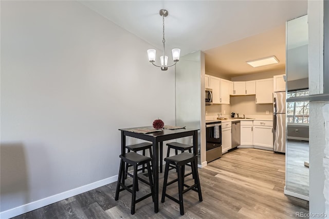 kitchen with pendant lighting, light hardwood / wood-style flooring, appliances with stainless steel finishes, white cabinetry, and a chandelier