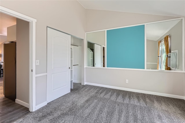 unfurnished bedroom featuring dark colored carpet, vaulted ceiling, stainless steel fridge, and a closet