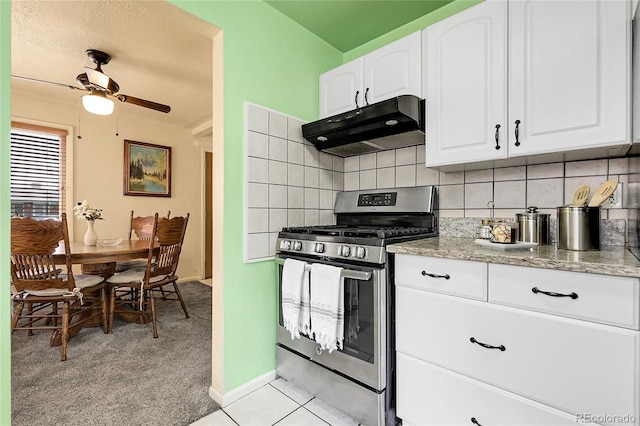 kitchen with ceiling fan, light stone counters, stainless steel gas range oven, white cabinetry, and under cabinet range hood
