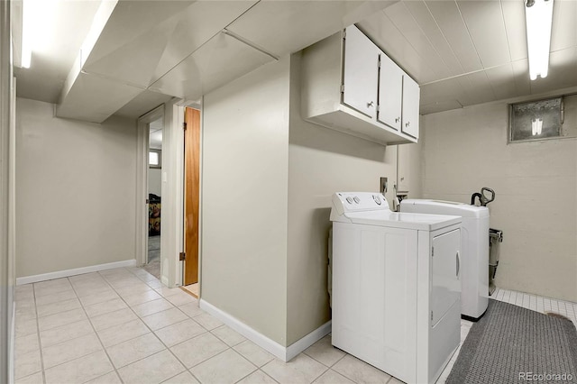 clothes washing area featuring baseboards, washing machine and dryer, cabinet space, and light tile patterned flooring