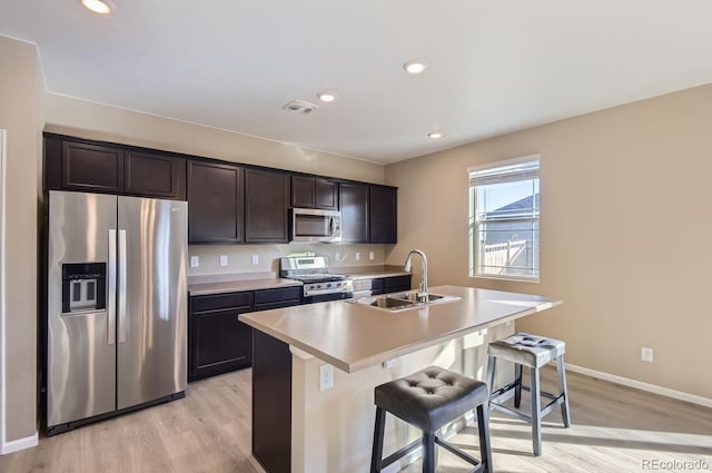 kitchen featuring appliances with stainless steel finishes, a breakfast bar, sink, a center island with sink, and light wood-type flooring